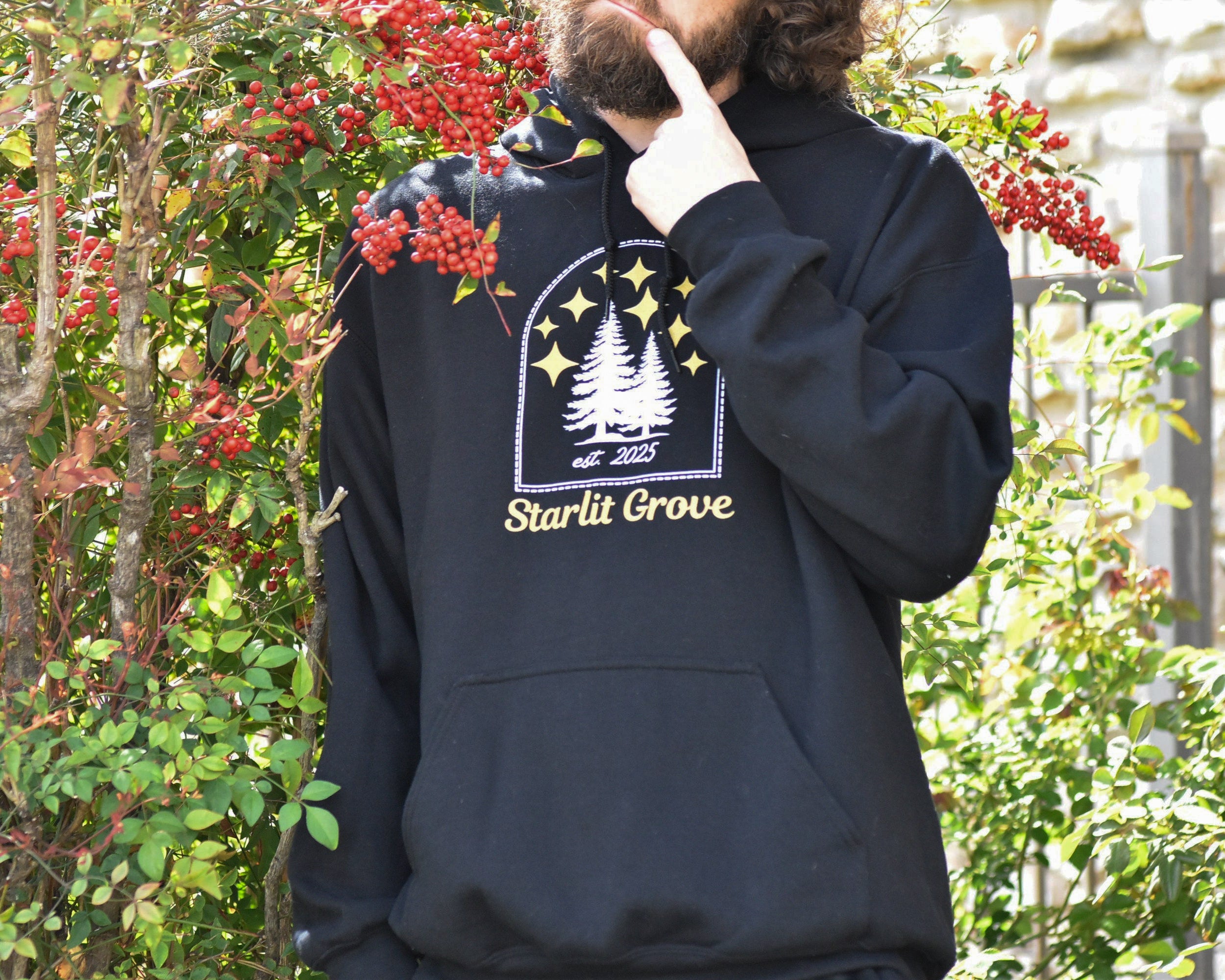 Person wearing a black hoodie with 'Starlit Grove' design in a natural setting