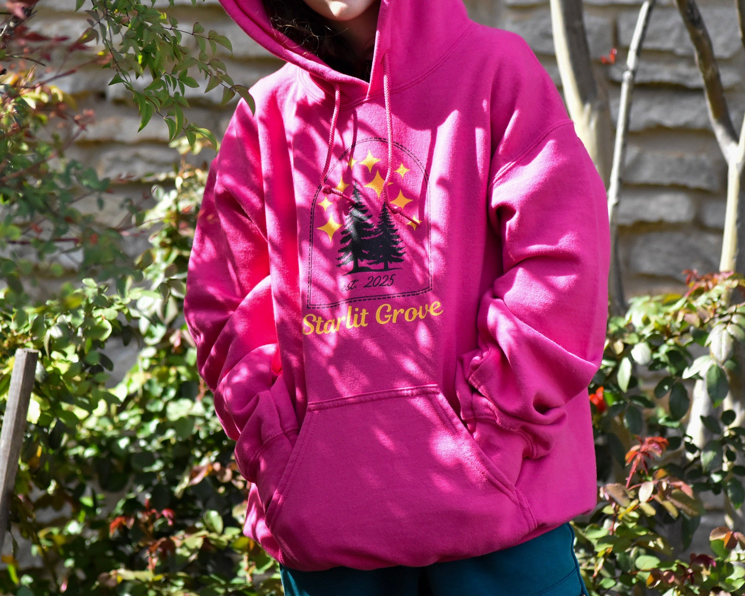Person wearing a pink hoodie with a logo and text, standing outdoors.