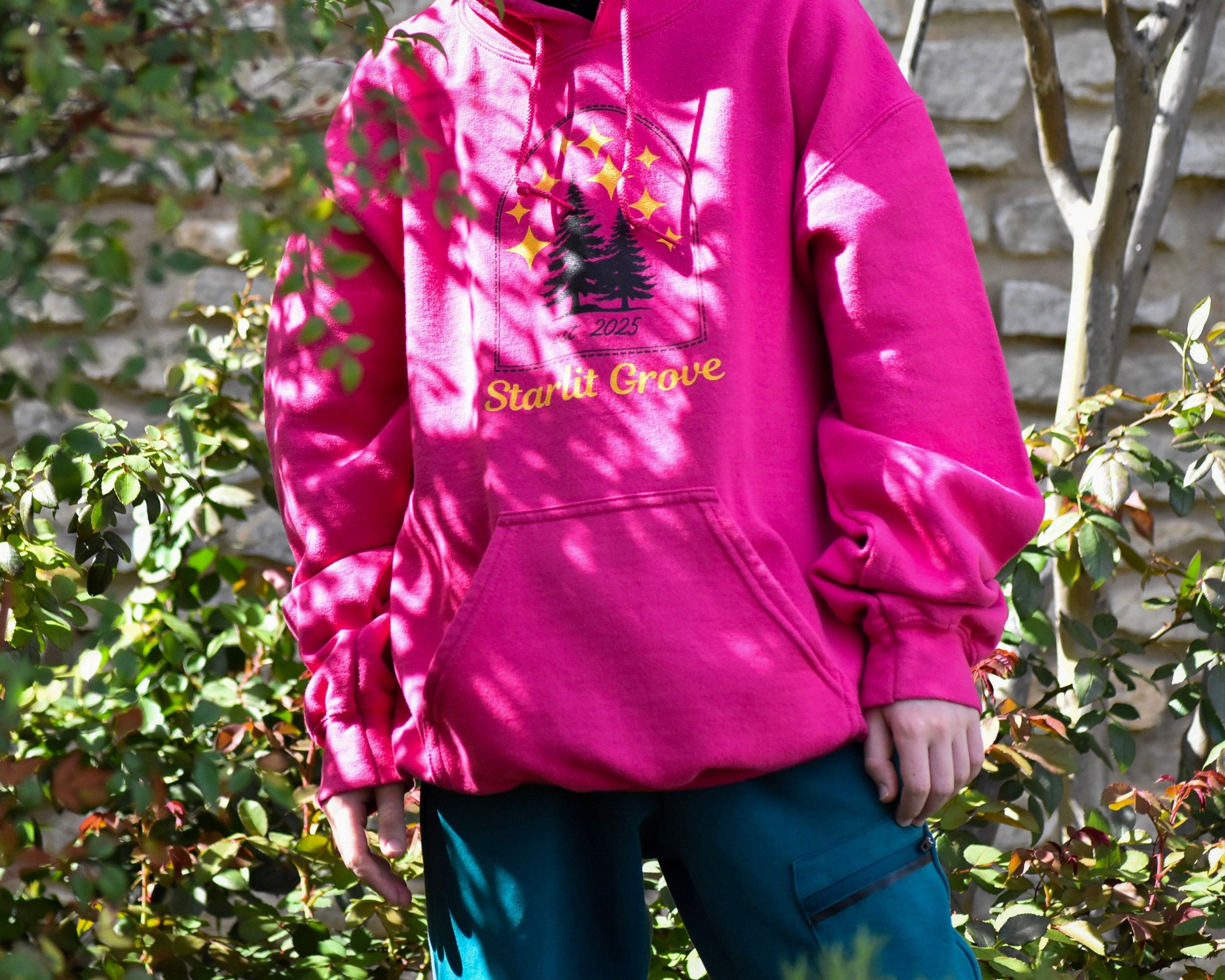 Person wearing a pink hoodie with a graphic design and text, standing outdoors.