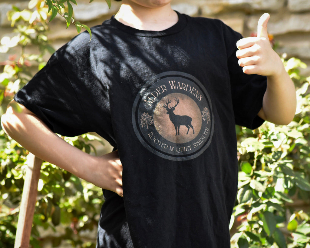 Person wearing a black t-shirt with a deer logo and text, giving a thumbs-up outdoors.