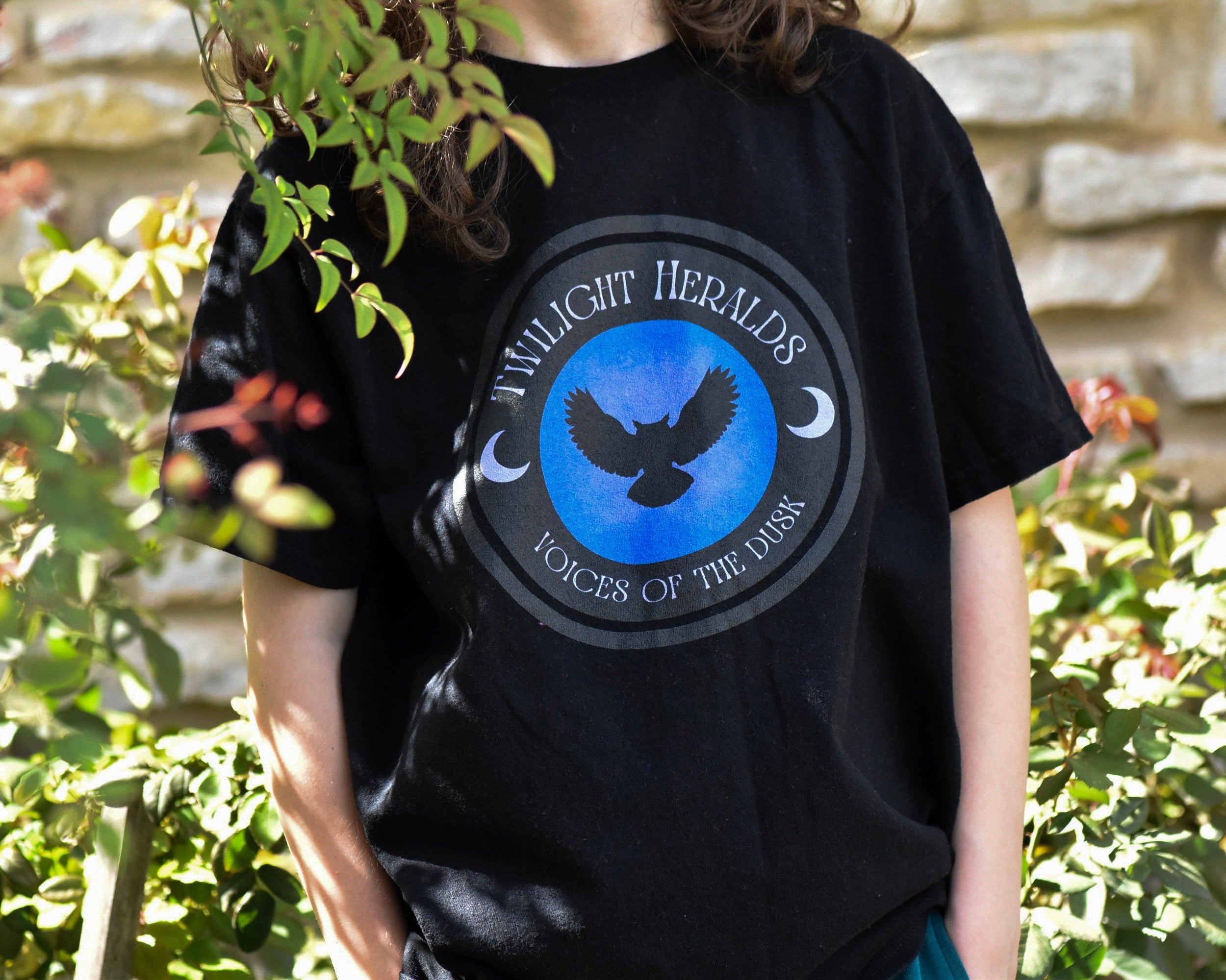 Person wearing a black t-shirt with a blue logo and text, standing outdoors.