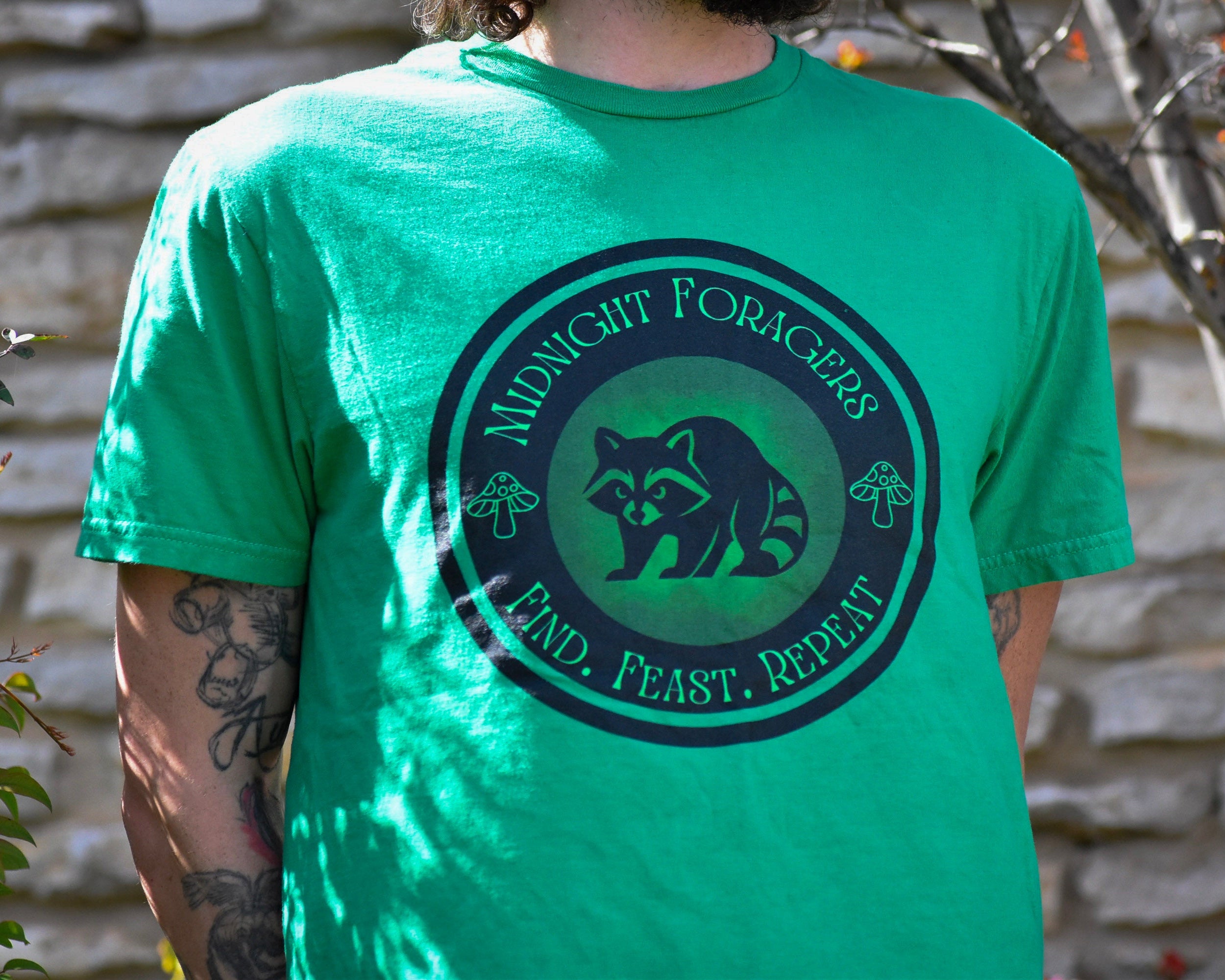 Person wearing a green t-shirt with a logo and text, standing outdoors.