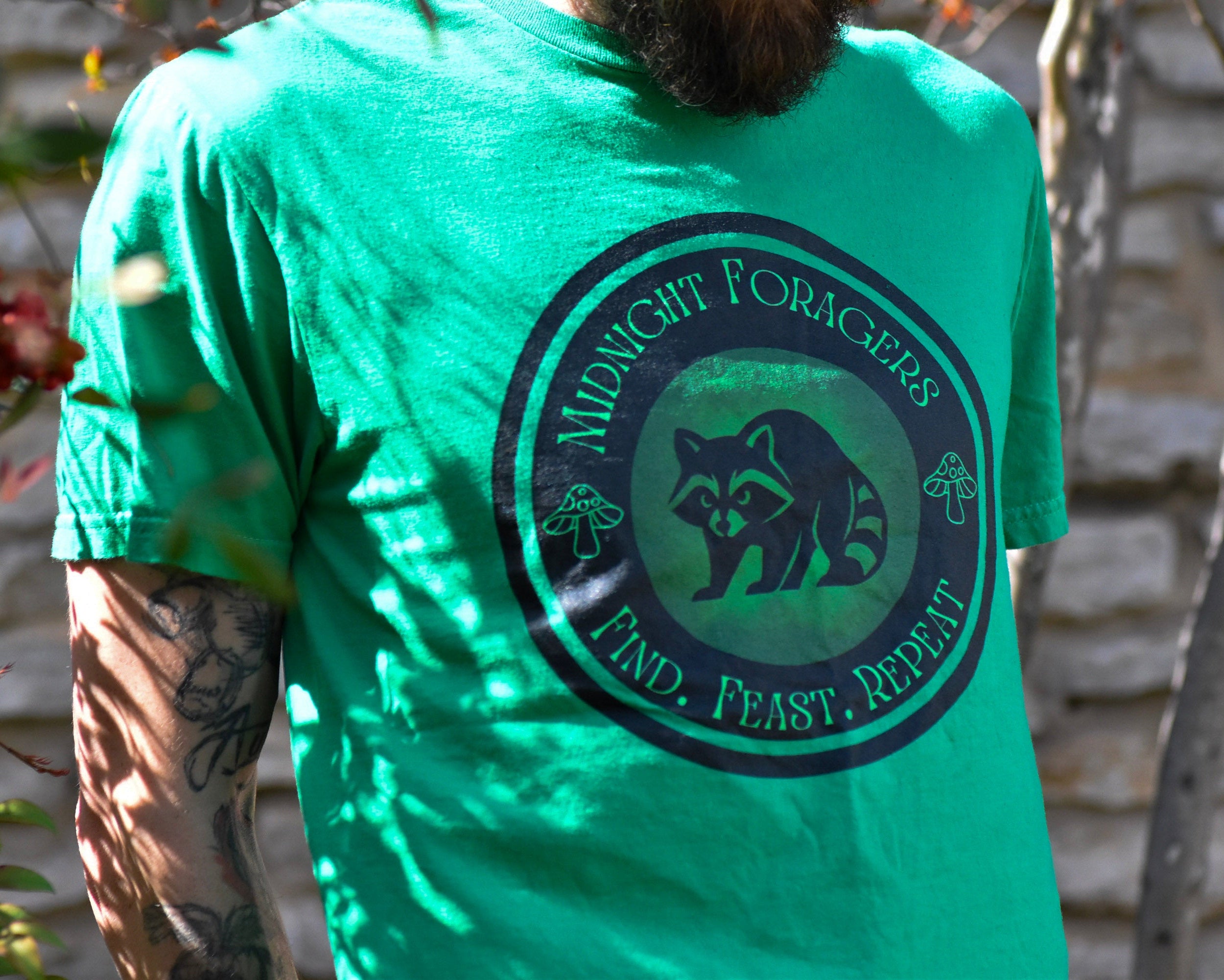 Person wearing a green t-shirt with a raccoon logo and text, standing outdoors.