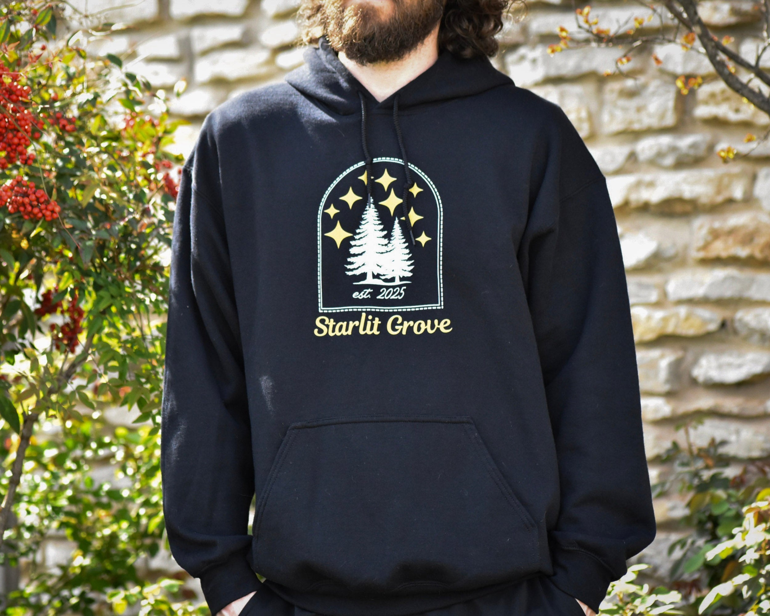 Person wearing a black hoodie with 'Starlit Grove' design outdoors.