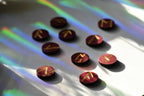 Red wooden circles with gold painted runes arranged on a white surface with rainbow lights.