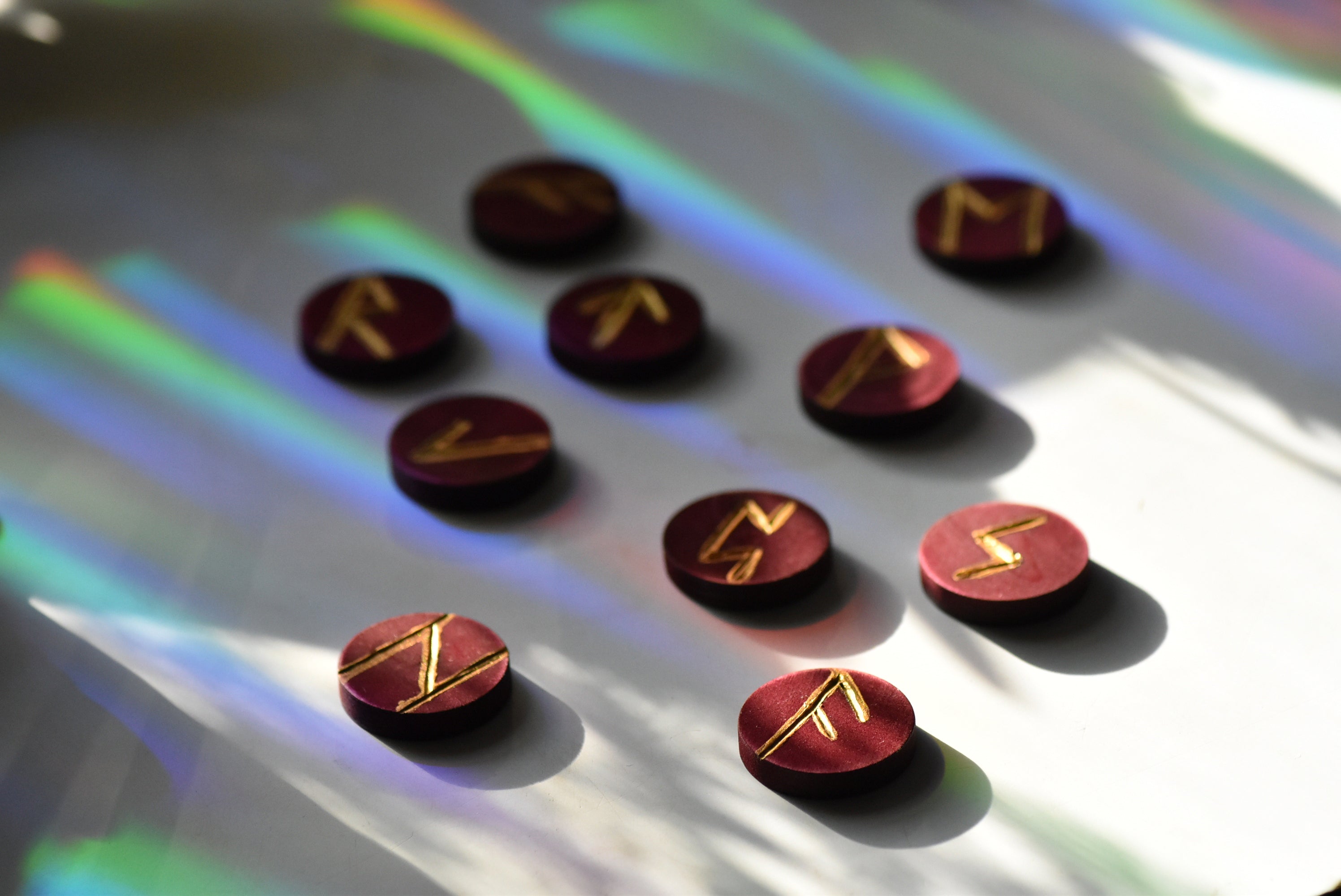 Red wooden circles with gold painted runes arranged on a white surface with rainbow lights.