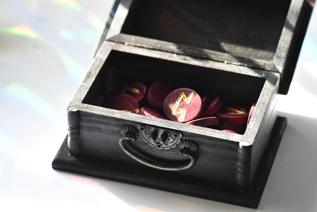 Black jewelry box with a silver handle containing red and gold wooden circle runes on a white background.