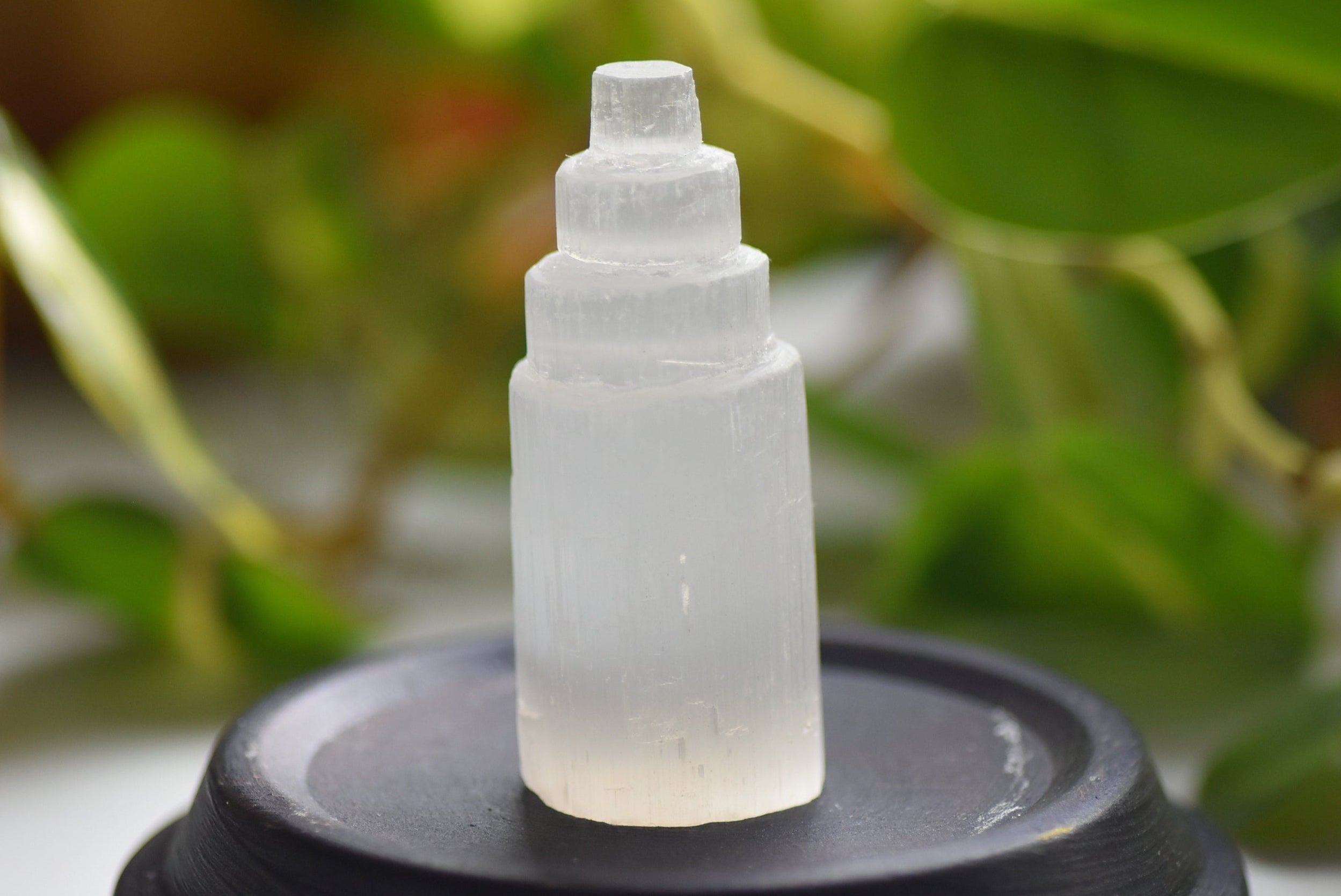 Frosted glass stone tower on a black stand with green foliage in the background