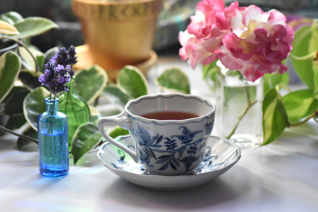 Teacup with floral design on a saucer, surrounded by flowers and greenery
