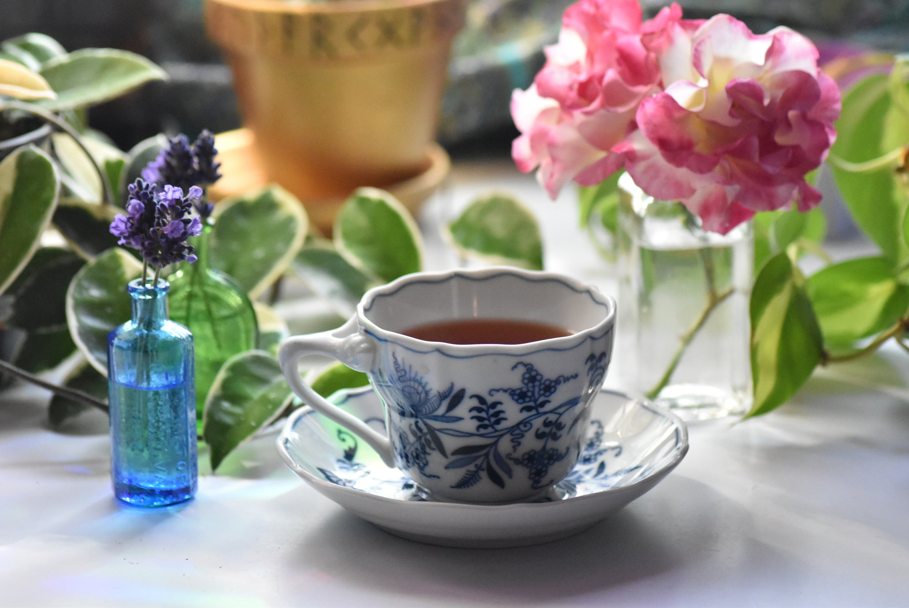 Teacup with floral design on a saucer, surrounded by flowers and greenery