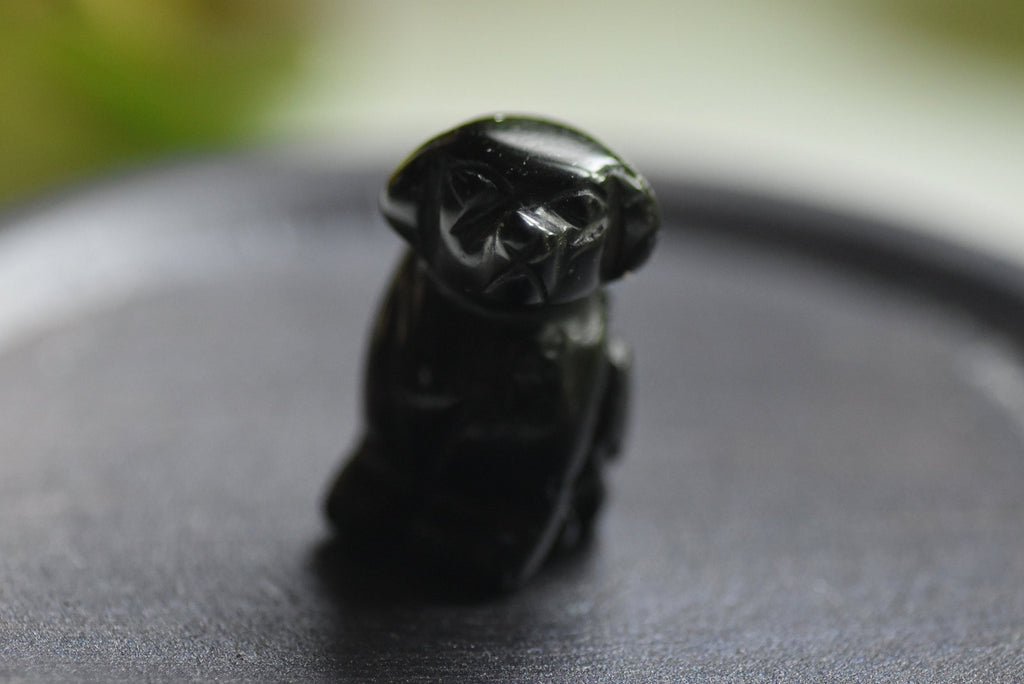 Black figurine of a dog on a dark surface with a blurred green background