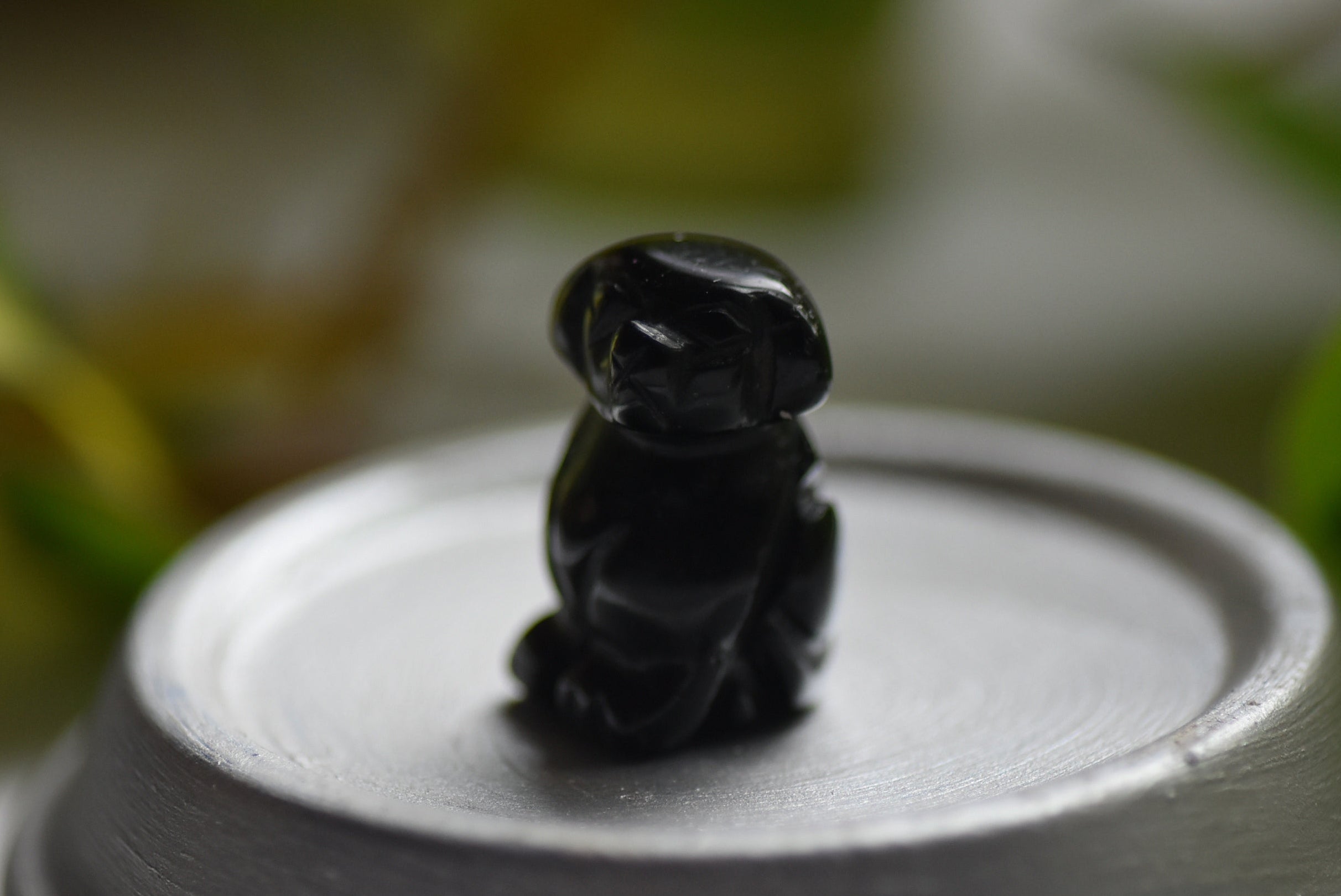 Black dog figurine on a light surface with a blurred green background