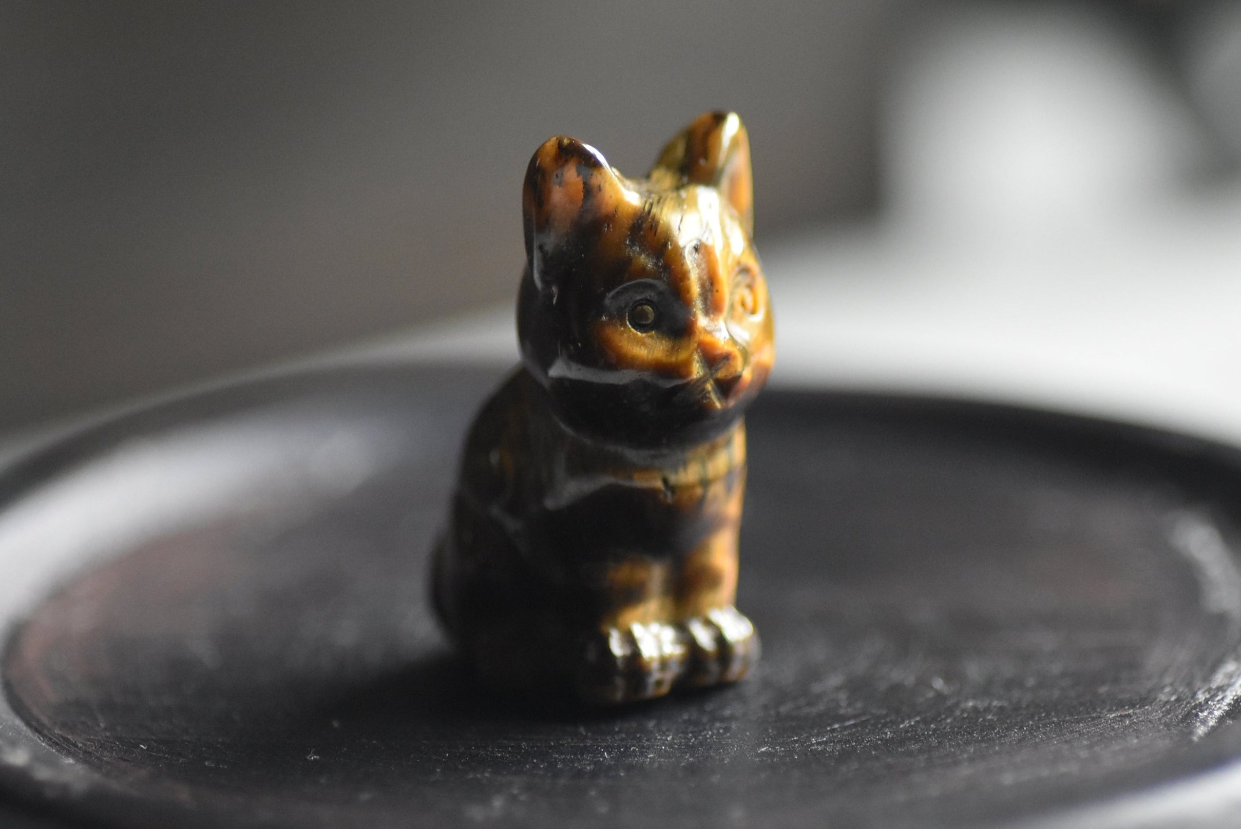 Small tigers eye crystal figurine carving of a cat on a dark surface with a blurred background.