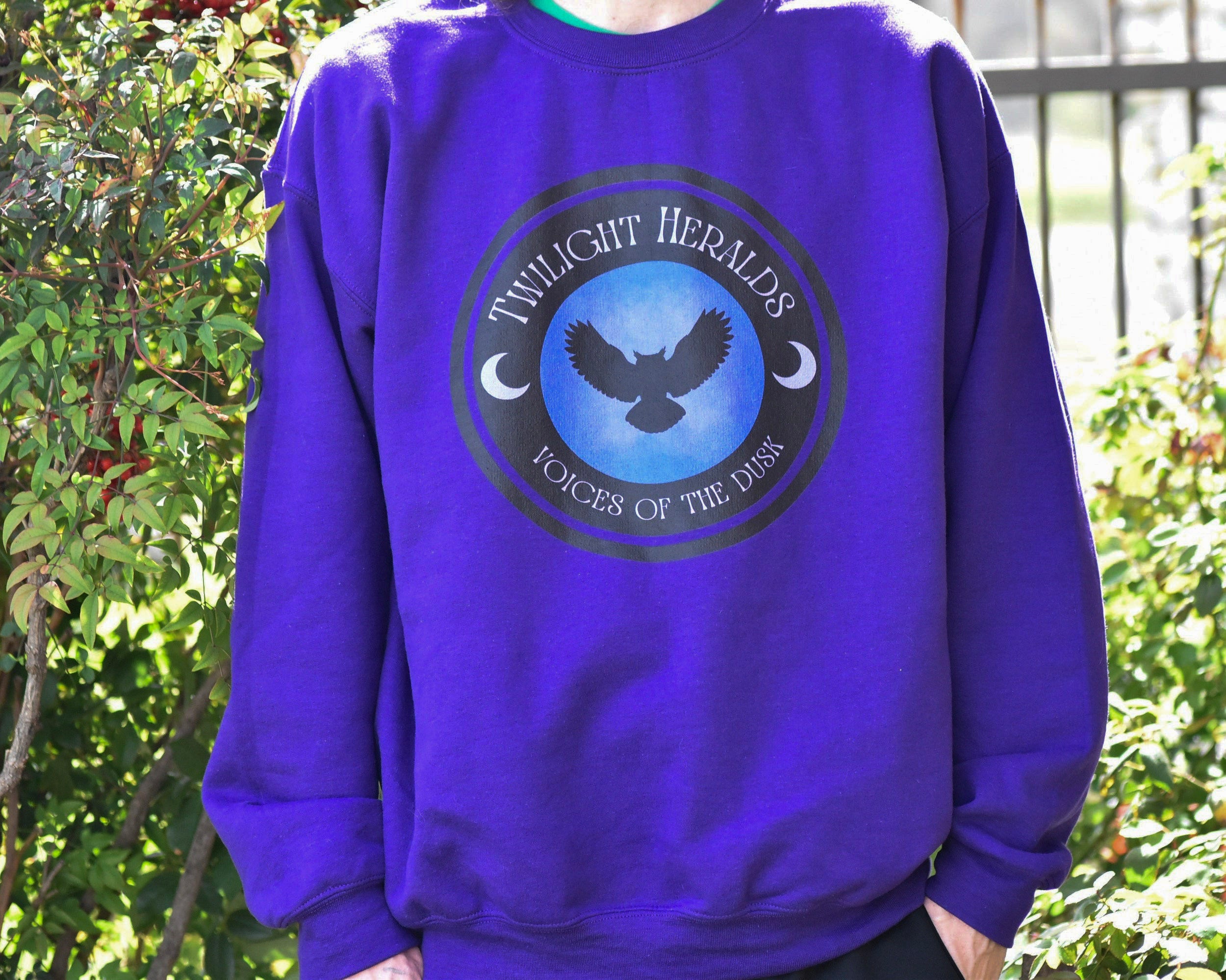 Person wearing a purple sweatshirt with a logo and text in an outdoor setting