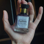 A hand holding a bottle of Persphone's Equinox Eau de Parfum, with a beaded bracelet visible on the wrist against a dark background.